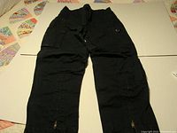 Full view of black heavy duty riding pants laid flat showing multiple pockets and zipper details.