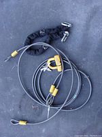 Photo of two steel security cables, one with black fabric sleeve, showing yellow end caps connected with carabiner-style clip.