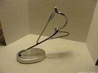 Front and side views of a polished aluminium abstract lady sculpture showing smooth, curved lines and minimalist style on oval base.