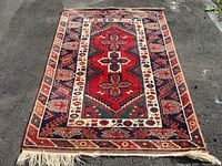 Full view of the Persian rug showing the central design and borders, laying flat on pavement.