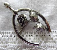 Front view of the Bond Boyd sterling silver wishbone brooch with rose and leaves shown on a lace fabric background.