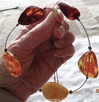 Close-up held view showing five large polished amber stones in different colors on a thin wire string with sterling silver clasp.