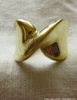 Close-up photo of gold plated sterling silver ring with criss cross design on a light fabric background.