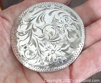 Front view of large round sterling silver brooch showing detailed floral and scroll engraving on front surface.