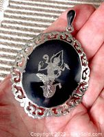 Handheld view of the pendant showing the engraved dancing Hindu princess on black niello background and detailed pierced sterling silver border.