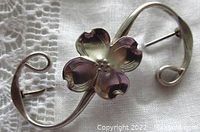 Top view of the polished sterling silver engraved dogwood flower brooch with curved stems on fabric background.