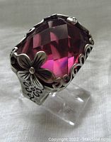 Front angled view showing large faceted rectangular pink glass stone set in sterling silver with floral openwork design and hammered shank.