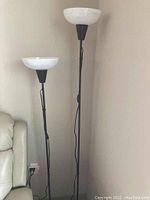 Photo showing two standing lamps of different heights with black poles and white bowl-shaped shades, positioned beside a beige couch.