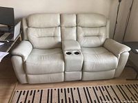 Front view of light grey leather reclining loveseat showing tufted cushions and center console