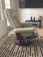 Side view of beige leather reclining swivel chair with wooden circular base