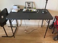 Photo showing a black folding table with adjustable height legs placed against a wall with decor items on top, illustrating condition and features.