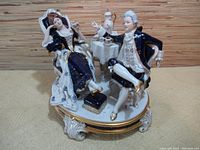 Shot of large Royal Dux figurine with man and woman seated beside small table with teapot and cups, showing detailed colors and poses.