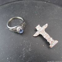 Two items on black surface: a silver basketball championship ring with an oval blue stone, and a silver totem pole pin marked 'Canada'
