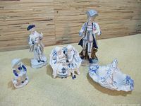 Five blue and white ceramic figurines on yellow surface against bamboo background showing standing and seated figures.