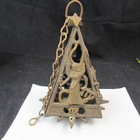 Front angle showing triangular brass votive holder with a three-dimensional angel figure and attached hanging chain, with star details at corners.