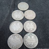 Lot of seven Canadian silver 25 cent coins arranged on black cloth, showing obverse details and wear.