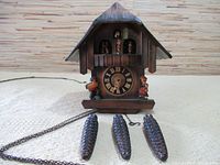 Front view of wooden chalet cuckoo clock with three pinecone weights and chain