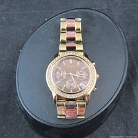 Full view of DKNY wristwatch with gold and rose gold metal link bracelet, rhinestone bezel and brown face with chronograph subdials.