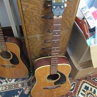 Full view of the 12-string acoustic guitar showing natural wood finish, body, neck and partial headstock, alongside another acoustic guitar.