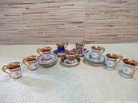 Overview of seven small porcelain cups with matching saucers, displayed in a row showing different designs and gold accents