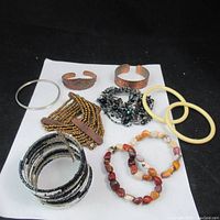 Photo showing full lot of 10 bracelets arranged on white paper against black background, illustrating variety of materials including copper, plastic, beads, and stones.
