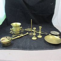 Full view of the lot showing all brass items including mortar and pestle, candle holders, snuffer, small dish, and incense burner on black backdrop.