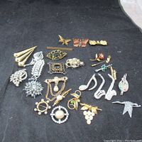 Full collection of vintage and antique brooches and pins laid on a black fabric background, showing variety of shapes and designs.