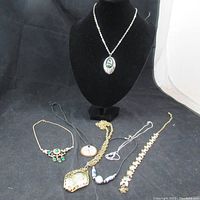 Full view of seven necklaces laid out with black background, showing variety of styles and pendants