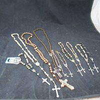 Full lot overview showing nine prayer bead rosaries with cross pendants on black background.