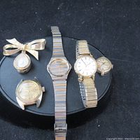Photo shows five vintage watches arranged on black surface, showcasing variety of watch bands and dial styles including metal and leather bands.