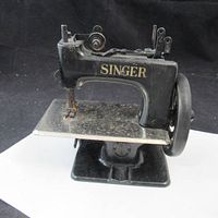Front angle photo showing the small black Singer sewing machine on base with handwheel and sewing area plate.