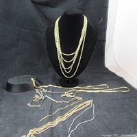Full display showing multi-layered chain necklace on black bust and several chains laid flat including a silver-tone chain.