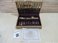 Full set of brass Dirilyte tableware displayed in open vintage case showing knives, forks, spoons and serving pieces.