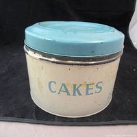 Exterior view of vintage metal cake tin with blue lid and 'CAKES' label, showing signs of age and wear.