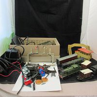 Overall view of vintage electric train set components including multiple train cars, tracks, transformer, and accessories displayed on a black surface.