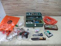 Overview of various fishing tackle items including lures, hooks, knife, reels, plastic bags with small items, and a wooden box.