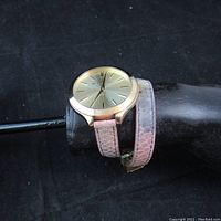 Michael Kors women's double-wrap wristwatch displayed on black stand, showing gold-tone dial and textured pink leather strap.