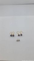 Two pairs of brass garnet earrings and one pair of sterling silver Pepsi bottle cap stud earrings on white background.