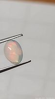 Close-up photo of the oval Ethiopian opal cabochon gemstone held with tweezers showing translucent body and color play.