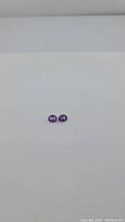 Two small deep purple oval amethyst gemstones displayed on white background