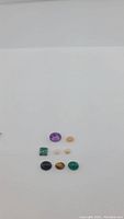 Overview photo showing nine polished natural gemstones arranged in three rows by color and shape on a white background.
