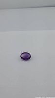Single oval faceted deep purple amethyst gemstone on white background, showing color and cut from top angle