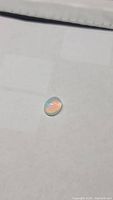 Oval cabochon cut Ethiopian opal with visible green and blue flashes on translucent body.