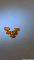 Five orange Fanta fire opal oval cabochons arranged on a white surface under light, showing smooth polished domed shape and internal fire.
