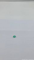 Photo showing the oval cut Zambian emerald gemstone from a distance on a white background.