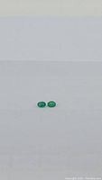 Front view of two small oval-shaped natural Zambian emeralds on plain white background showing size and color.
