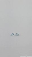 Two pear cut aquamarine gemstones displayed side by side on a neutral surface, showing clarity and color from front angle.