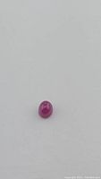 Oval polished natural ruby cabochon against a white background.