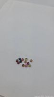 12 small round cabochon cut tourmaline stones in various colors on white background.