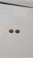 Two small oval cabochon stones with dark amber body tone, studio close-up, flat lay.